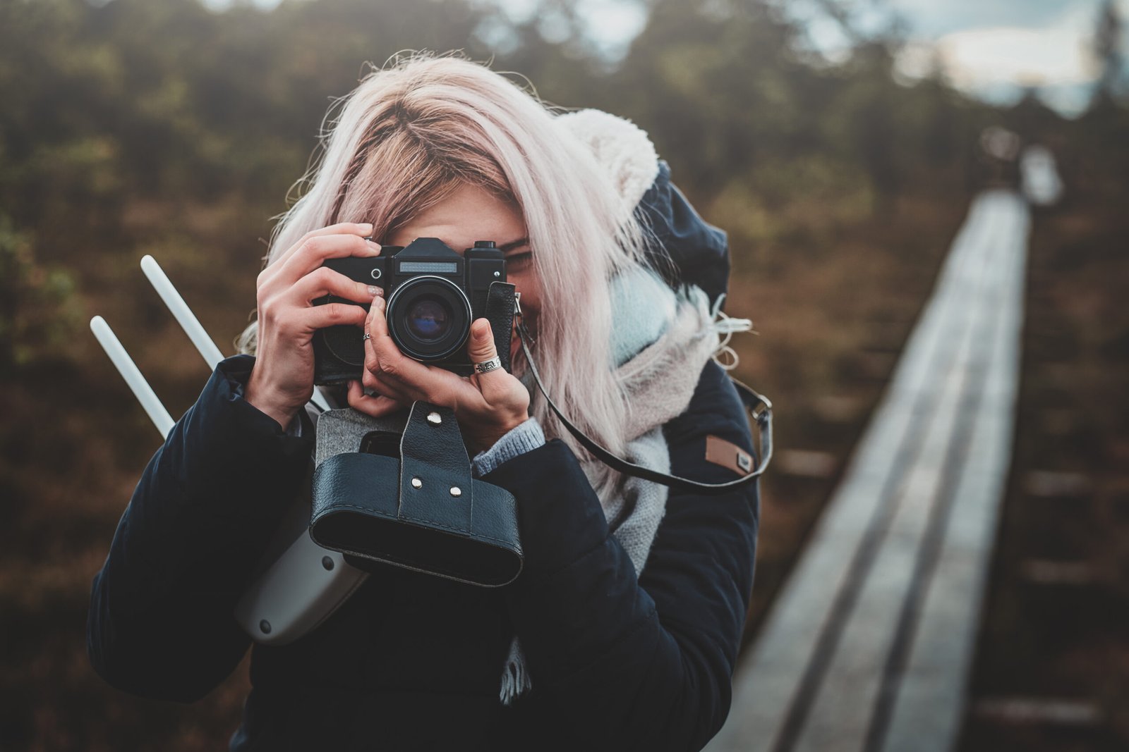 Focused blonde girl is making a photo with her photo camera while walking in the park.